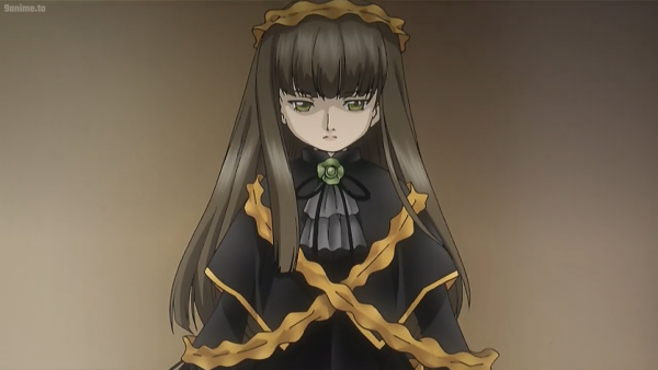 A doll with long brown hair, light skin, hazel eyes, and frilly orange headdress and matching orange frills criss-crossing down her black dress and orange-hemmed capelet, sitting on a shelf from the dollmaker's shop in the second season of Rozen Maiden. Her grey jabot has a thin black bowtie and an ornament which matches her eye colour.
