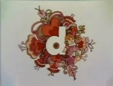 The doll sitting next to a lowercase d, surrounded with flowers, while three butterflies fly over to rest around it. The gif is then reverse-looped, so the butterflies fly back off-screen.