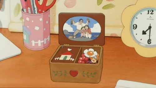 A close-up of Hiromi's desk, including her cherished early childhood photograph of the last time she, her father, and her mother all spent a nice day out together by the sea... it's framed in a little wooden jewelbox filled with trinkets. A flower-shaped analogue clock sits at the edge of the screen, and a pink cup with a stylized blue and white house, white picket fence, and what might be stylized snowflakes showering down... the cup carries scissors, pens, and a box cutter.